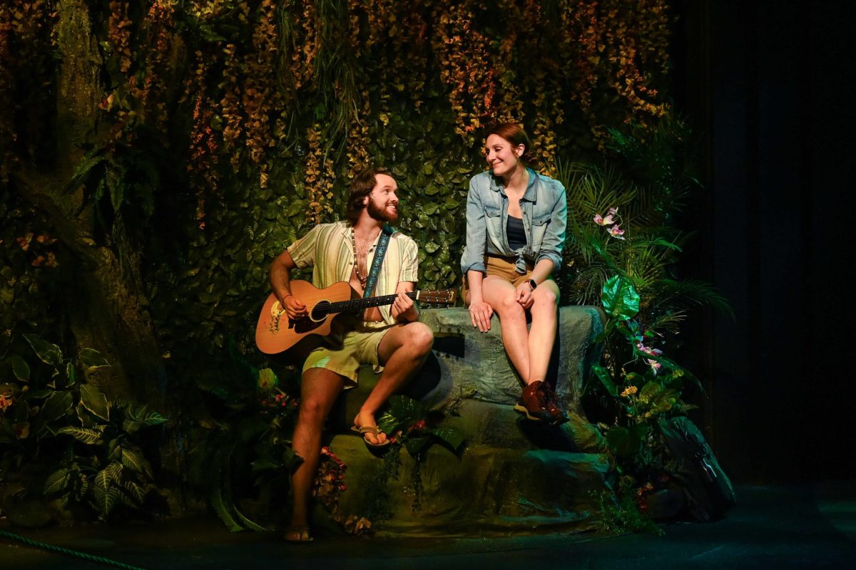 A man and woman sit on a rock and smile at each other.