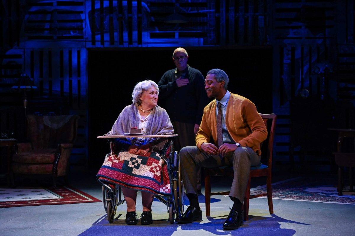 Two elderly individuals smile at each other while someone looks on.